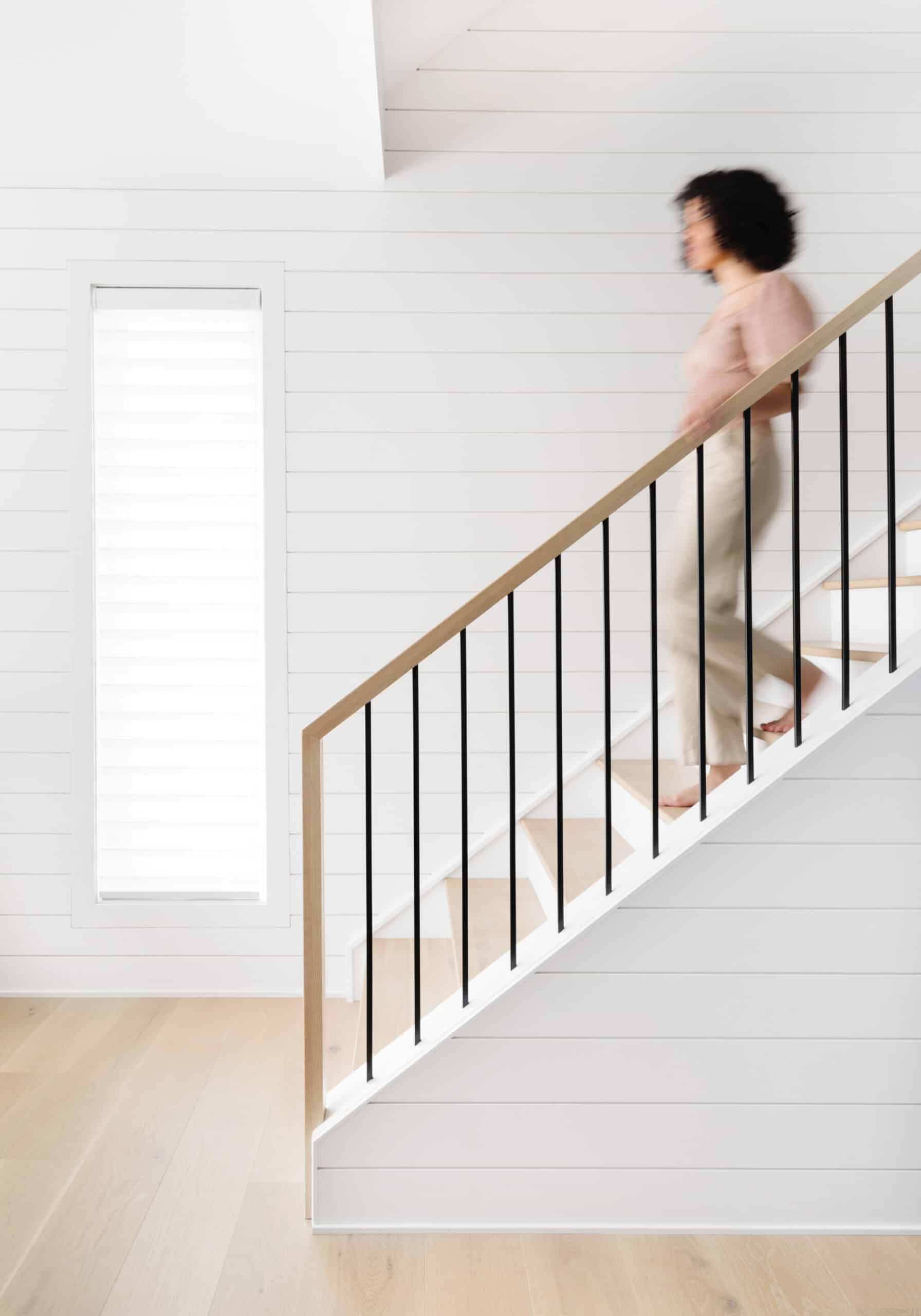 A woman walking up the stairs in a white house.