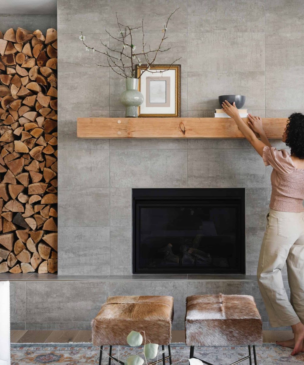 A woman is putting logs on a fireplace mantel.